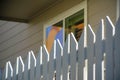 Shady white picket fence with sun cresting on edge of wood or timber with suburban beige house background in late