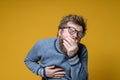 Shaggy, bearded man with glasses and an old sweater coughs, covers mouth with palm and holds hand on chest, experiencing Royalty Free Stock Photo