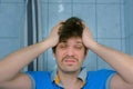 Shaggy young man with headache hangover in bathroom at morning rubs his face.