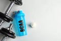 Shaker with abbreviation BCAA Branched-chain amino acid, dumbbells and powder on white table, flat lay. Space for text