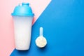 Shaker and scoop with protein on pink and blue background, copy space Royalty Free Stock Photo