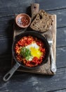 Shakshouka eggs in vintage pan on rustic wooden cutting board on a dark background. Royalty Free Stock Photo