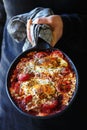 Shakshouka - Middle eastern traditional dish with poached eggs in tomato sauce, man holding pan