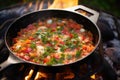 shakshuka being cooked on an outdoor campfire grill