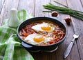 Shakshuka or fried eggs in tomato sauce with red bell pepper in a serving cast-iron frying pan on a wooden background Royalty Free Stock Photo