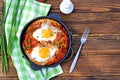 Shakshuka or fried eggs in tomato sauce with red bell pepper in a serving cast-iron frying pan on a wooden background Royalty Free Stock Photo