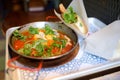 Shakshuka at pan on tray in cafe of Israeli cuisine. Shakshouka is fried eggs with tomatoes, vegetables and herbs Royalty Free Stock Photo