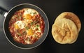 Shakshuka - poached eggs in tomato sauce, onion, pepper and spices in iron pan with pita bread on dark wooden background. Royalty Free Stock Photo