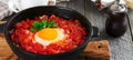 Shakshuka with tomato sauce and fried egg in a cast iron pan for breakfast on the old wooden background. Rustic Style, Selective Royalty Free Stock Photo