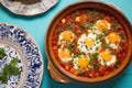 shakshuka in a white porcelain dish on a turquoise tablecloth