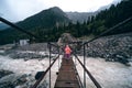 A shaky wooden bridge with metal cables. Stormy flow of a mountain river. Active recreation and hiking. Gloomy rainy weather.