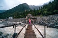 A shaky wooden bridge with metal cables. Stormy flow of a mountain river. Active recreation and hiking. Gloomy rainy weather.