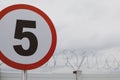 Shallow depth of field selective focus image with a speed limit traffic sign in front of a wall with razor wire on top, outside