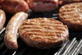 Shallow focus close up of tasty assorted delicious sausages and burgers sizzling and cooking on a barbecue griddle plate, outside Royalty Free Stock Photo