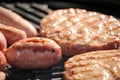 Shallow focus close up of tasty assorted delicious sausages and burgers sizzling and cooking on a barbecue griddle plate, outside Royalty Free Stock Photo