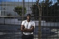 Shallow focus shot of an African-American male in a white shirt leaning on a fence with arms crossed Royalty Free Stock Photo