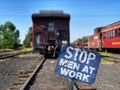 Shallow focus shot of a blue Stop Men at work Sign at Railroad Depot with blur trains