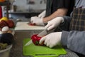 Shallow focus shot of people cutting red peppers in white gloves on a green board