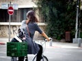 Shallow focus shot of a woman riding a bicycle with Boston terrier puppy placed on a green basket