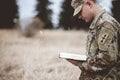 Shallow focus shot of a young soldier reading a bible in a field