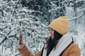 Shallow focus of a smiling female in a brown outfit looking at her mobile in snow-covered forest