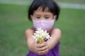 Shallow focus of a  Southeast Asian child girl wearing mask face offering a white jasmine flower Royalty Free Stock Photo