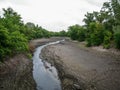 A shallow, polluted riverbed among the forest banks