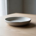A shallow, round ceramic plate rests on a light wood table. The plate has a smooth, Royalty Free Stock Photo