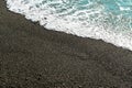 Shallow volcanic black sandy beach and pebbles, blue water waves and white foam washes the coastline with wet dark sand on the sea Royalty Free Stock Photo