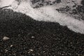 Shallow volcanic black sandy beach and pebbles, water waves and white foam washes the coastline with wet dark sand on the sea Royalty Free Stock Photo