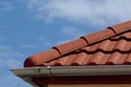 shallow zink eavestrough or gutter. red brown sandy textured modern concrete roof tiles in closeup