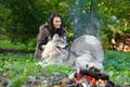 Shaman woman with an Alaskan Malamute next to the fire in the forest