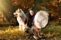 Shaman woman with an Alaskan Malamute drumming in the sunny forest by the fire