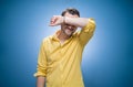 Shame. Young man covering face with hands over blue background, dresses in yellow shirt. Ashamed guy Royalty Free Stock Photo