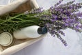 Shampoo bottle, aromatic candle and bunch of lavender flowers in wicker basket on white table background.