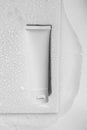 Shampoo, hair conditioner, hand cream lotion or facial cleanser in white plastic tube on glass with water drops, gentle soap foam