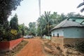 A dirt road going past a rustic mud hut with slanted roofs in a village in the