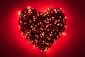 Shape of heart folded from tangled wires of a garland with red light bulbs on red background in the dark with a vignetting effect