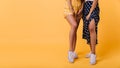 Shapely girls in white gumshoes standing on bright yellow background. Photo of female legs with tanned skin..