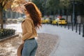 Shapely red-haired woman wears light-blue jeans posing in park. Outdoor photo from back of pretty girl in casual outfit