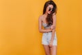 Shapely young woman in denim shorts smiling on yellow background. Studio portrait of stunning girl in sunglasses