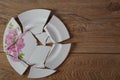 Shards of a broken plate on the wooden floor. Broken white ceramic plate on the wooden floor. Broken dishes. Top view of a damaged