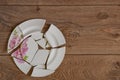 Shards of a broken plate on the wooden floor. Broken white ceramic plate on the wooden floor. Broken dishes. Top view of a damaged