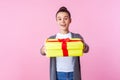 Share holiday present. Portrait of generous teenage brunette girl giving gift box to camera and smiling. pink background