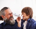 They share a love for aircraft. a young boy sitting on his grandfathers lap playing with a toy jet.