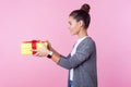 Share present. Side view portrait of generous teenage brunette girl giving gift box. pink background