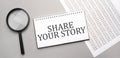 Share your story sign in white paper notepad and magnifying glass on the grey background