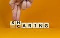 Sharing is caring symbol. Businessman turns wooden cubes and changes the word `sharing` to `caring`. Beautiful orange table,