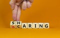 Sharing is caring symbol. Businessman turns wooden cubes with words `sharing is caring`. Beautiful orange table, orange backgrou