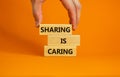 Sharing is caring symbol. Wooden blocks with words `Sharing is caring` on beautiful orange background. Businessman hand. Busines